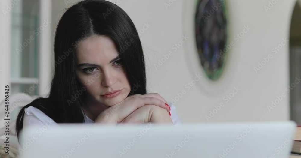 The girl reading from laptop, corrects her hair and looking on screen in home The girl reading from laptop, corrects her hair and looking on screen in home