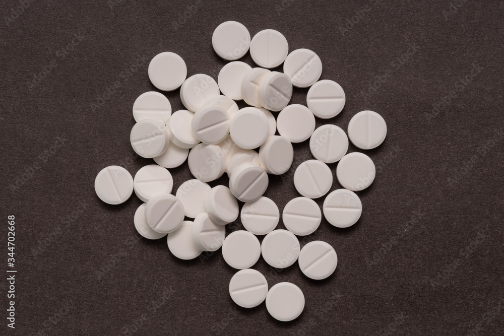 White tablets are scattered from a bottle on a brown background.