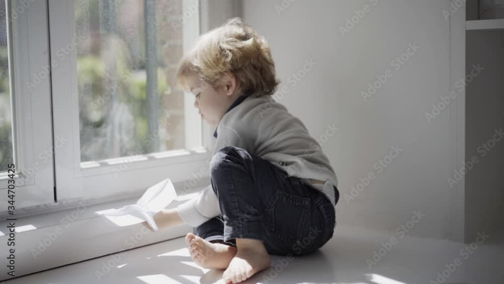 Happy little boy playing with paper plane on white windowsill at home Happy little boy playing with paper plane on white windowsill at home