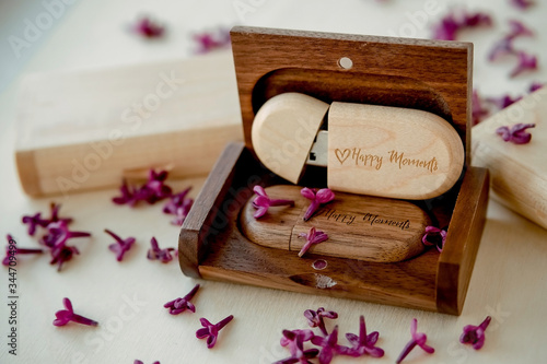 Fényképezés Wooden brown usb flash drives with boxes with the text Happy Moments with lilac petals on a white background, data storage, beautiful feedback to client