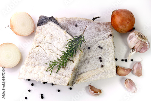dry salted raw cod isolated over white background, accompanied by pepper, onion, garlic, parsley, spices photo