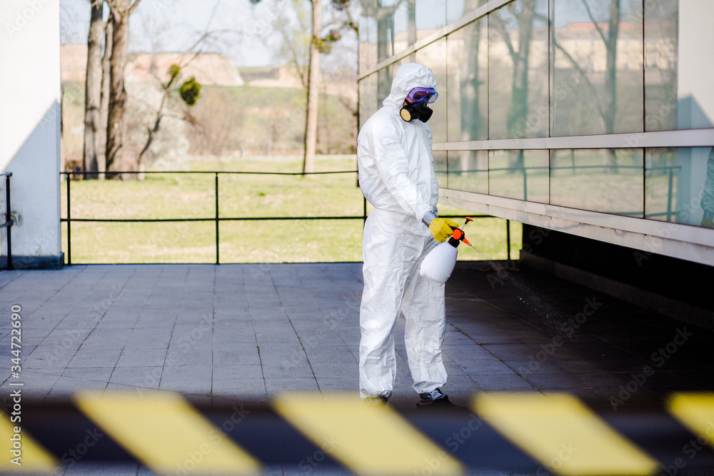 Stop coronavirus. Portrait of man in white protection suit with mask and sprayer holding arms up and celebrating successful city disinfection.