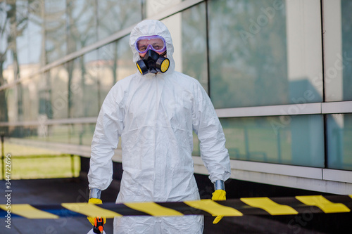 Stop coronavirus. Portrait of man in white protection suit with mask and sprayer holding arms up and celebrating successful city disinfection.