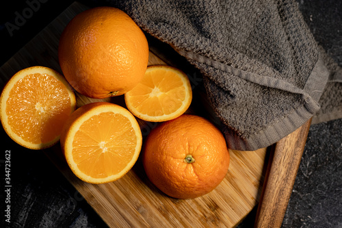 Overhead of sliced orange citrus fruit on a wooden board with a gray towel on a dark background.