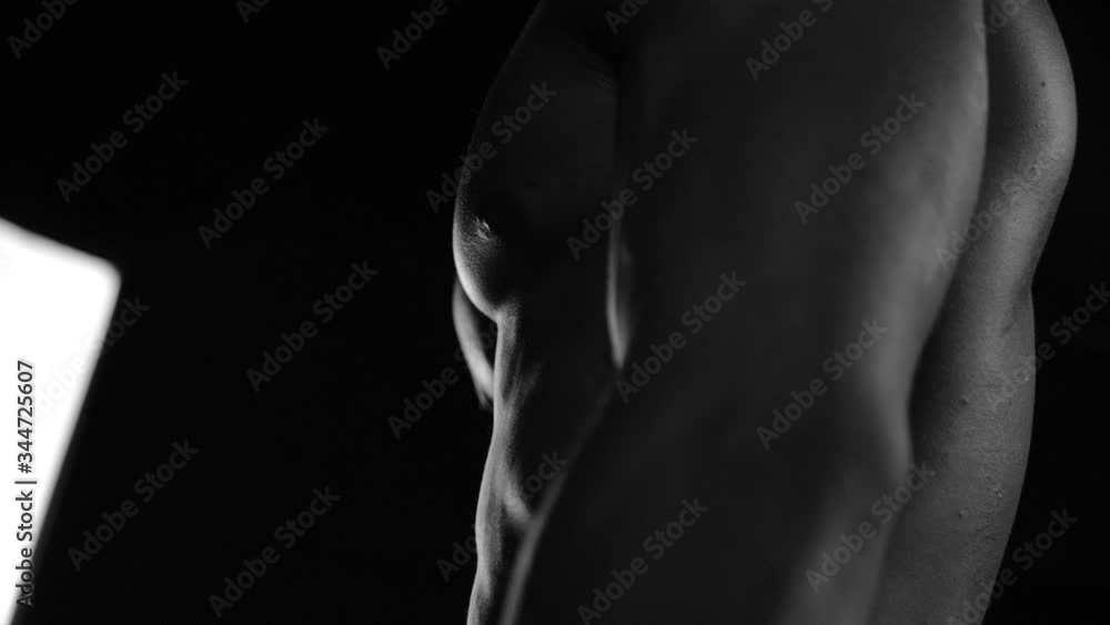Strong bodybuilder posing and training in contrast light showing his body and every muscle on it under water drops and slow rain Strong bodybuilder posing and training in contrast light showing his body and every muscle on it under water drops and slow rain