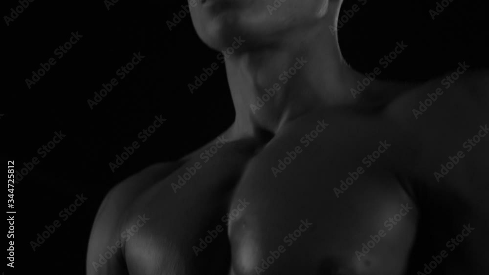 Strong bodybuilder posing and training in contrast light showing his body and every muscle on it under water drops and slow rain Strong bodybuilder posing and training in contrast light showing his body and every muscle on it under water drops and slow rain