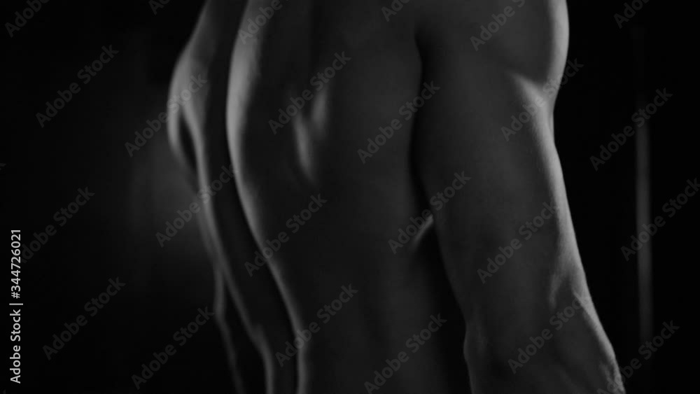 Strong bodybuilder posing and training in contrast light showing his body and every muscle on it under water drops and slow rain Strong bodybuilder posing and training in contrast light showing his body and every muscle on it under water drops and slow rain