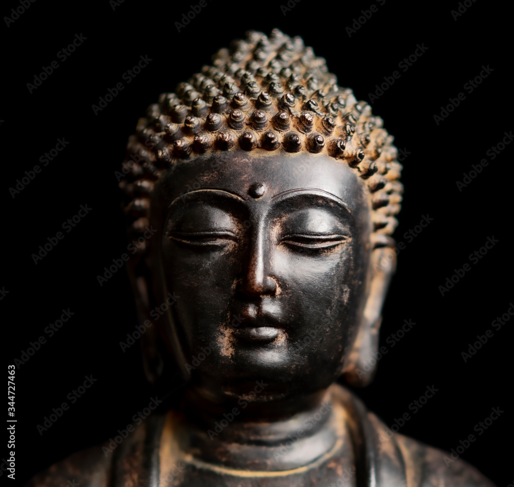 A small replica statue of the head of The Buddha isolated on black