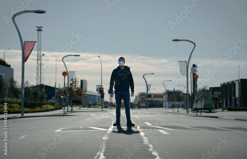 Young man wearing face mask standing in the middle of the road on an empty city centre. Coronavirus concept