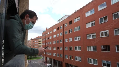 sick man covid-19 virus with mask peeking out the window using a smartphone
