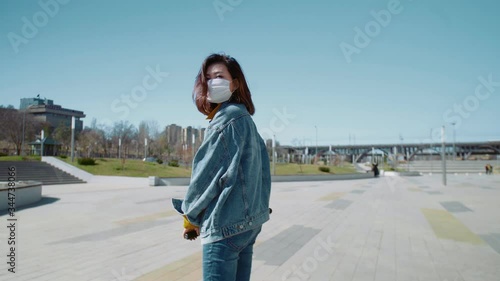 Back view of young woman in a jeans jacket rides the scooter in a summer park photo