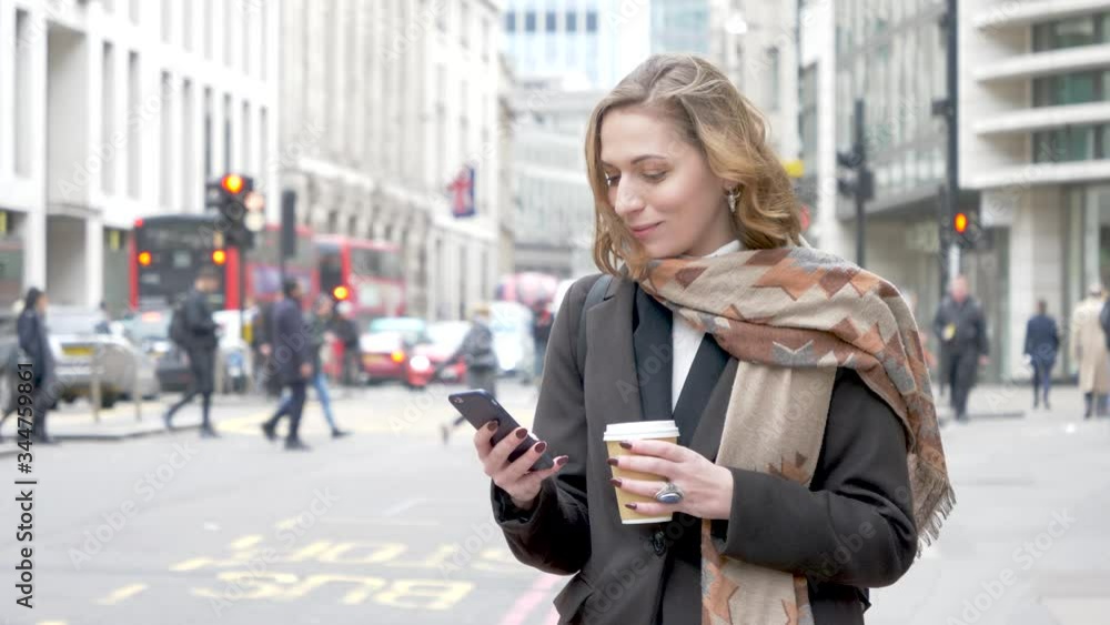 Blond woman using smartphone and holding coffee cup in London Blond woman using smartphone and holding coffee cup in London