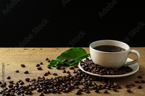 White coffee cup and coffee beans on wooden table with copyspace for text. Selective focus.