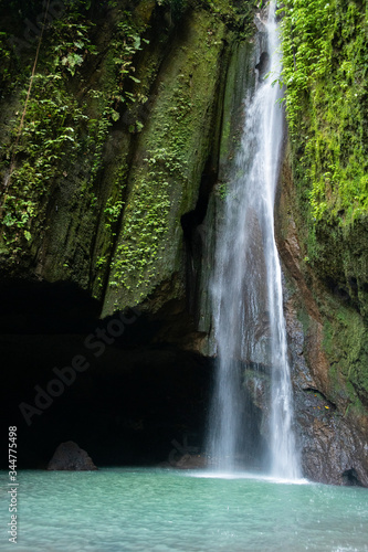 Fototapeta Naklejka Na Ścianę i Meble -  A waterfall falls beside a dark cave, pooling in a clear waterfall vault
