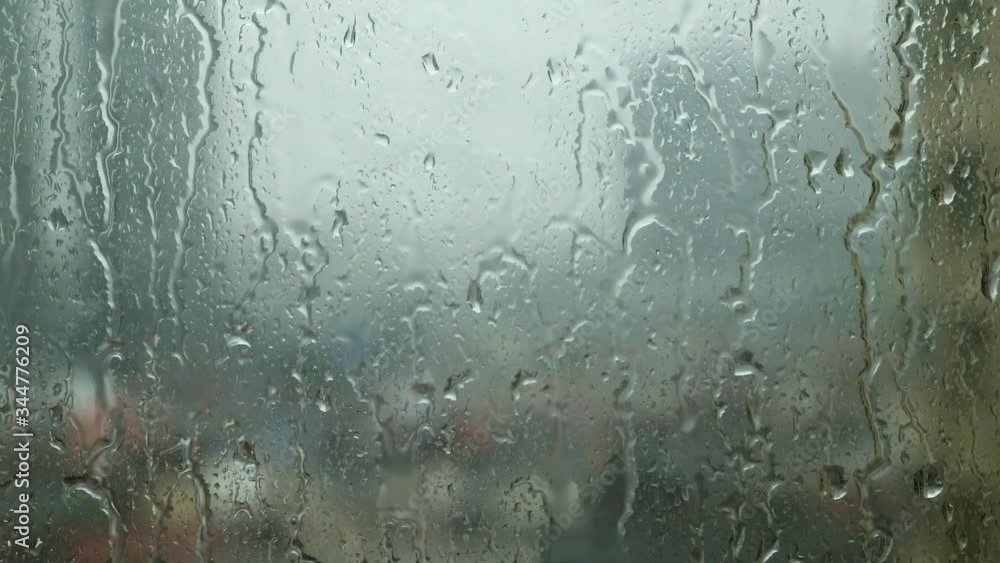 Closeup raindrops water droplets trickling down on wet clear window glass during heavy rain against blurred background cloudy backdrop in rainy day monsoon season Closeup raindrops water droplets trickling down on wet clear window glass during heavy rain against blurred background cloudy backdrop in rainy day monsoon season