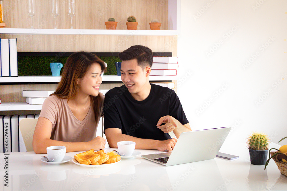Asian couple working together with laptop in morning and looking at each other. Breakfast and coffee on table. Asian couple working together with laptop in morning and looking at each other. Breakfast and coffee on table.