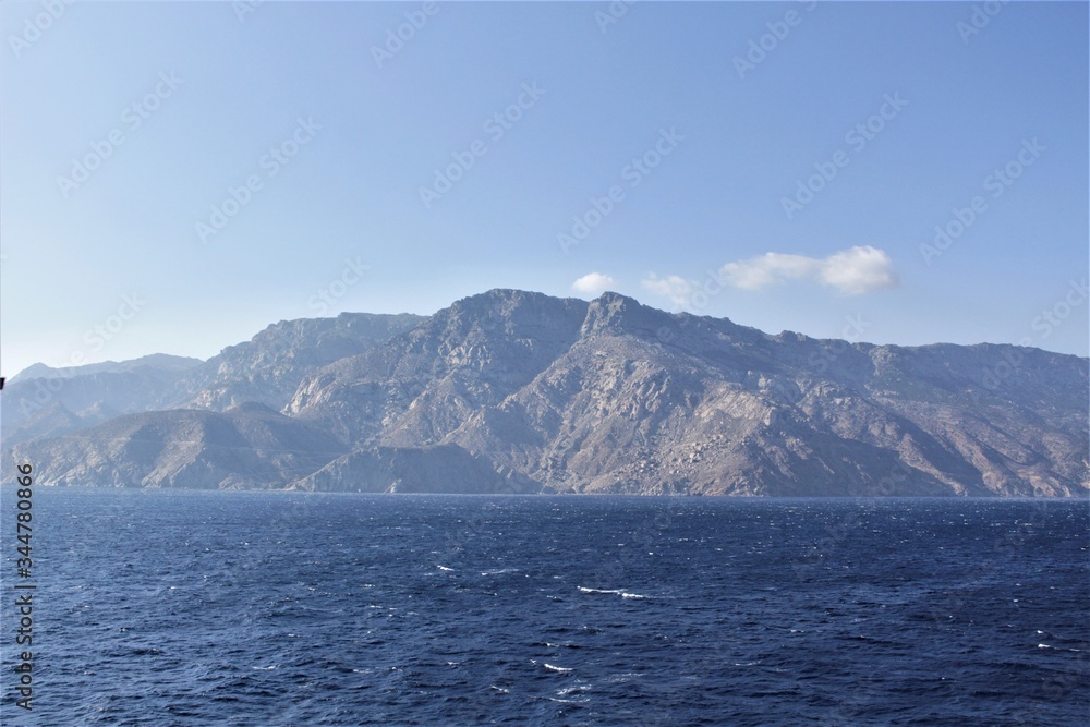 A deserted island lies in the waters of the Mediterranean Sea, its mountains and coastline are visible from far away.