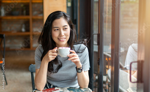 Young beautiful girl holding a cup of coffee in cafe. Outdoor portrait of young beautiful woman posing while traveling holiday vocation. Girl with coffee. Female traveler, Asian women drinking coffee.
