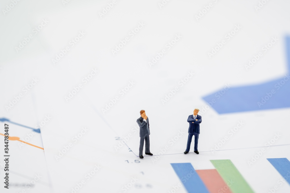 Two businessman miniature people figures meeting on graph report paper background with copy space. Using as business, financial, money and cooperation concept. Two businessman miniature people figures meeting on graph report paper background with copy space. Using as business, financial, money and cooperation concept.
