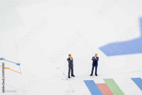 Two businessman miniature people figures meeting on graph report paper background with copy space. Using as business, financial, money and cooperation concept.