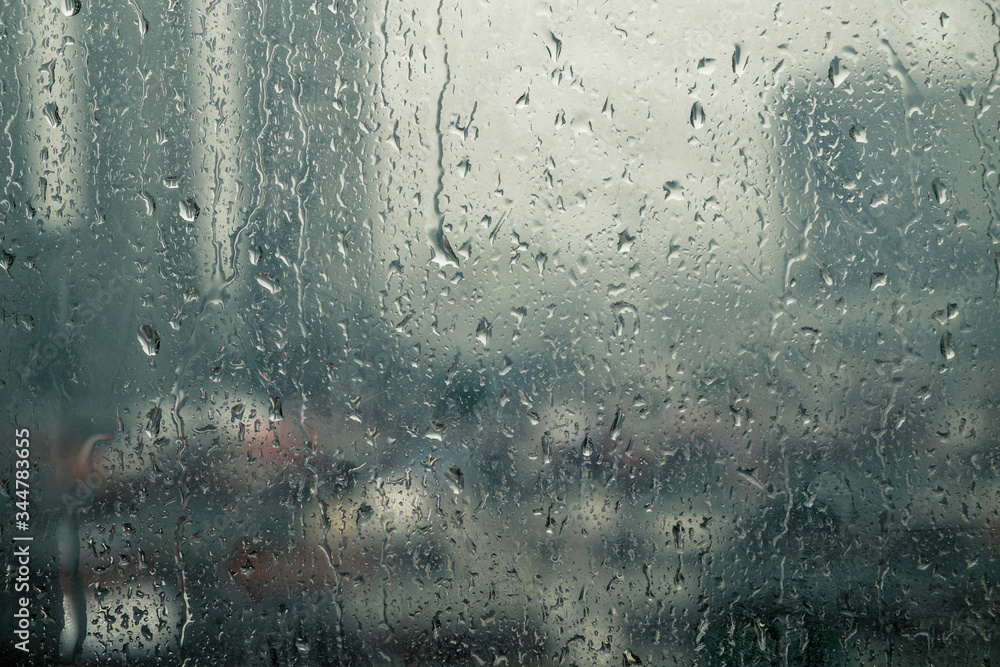 Closeup raindrops water droplets trickling down on wet clear window glass during heavy rain against blurred city view in rainy day monsoon season Closeup raindrops water droplets trickling down on wet clear window glass during heavy rain against blurred city view in rainy day monsoon season