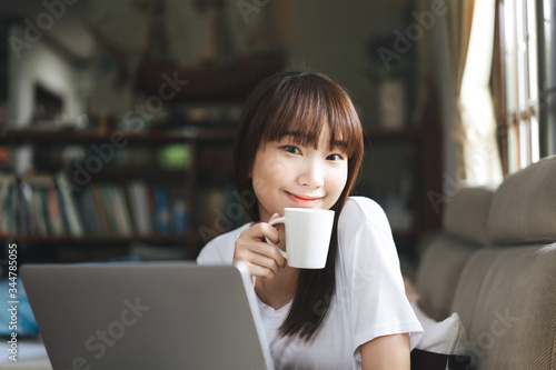Asian teenager woman work and study online via internet at home hold coffee cup.