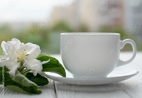 Hot tea in white porcelain cup with white flowers on a branch of apple on a white wooden background