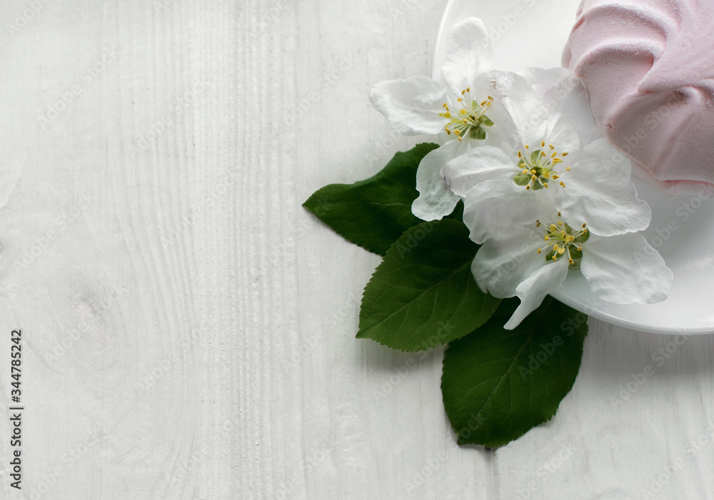 Pink marshmallows on a white porcelain plate Branch with white flowers of apple trees on white wooden background Pink marshmallows on a white porcelain plate Branch with white flowers of apple trees on white wooden background