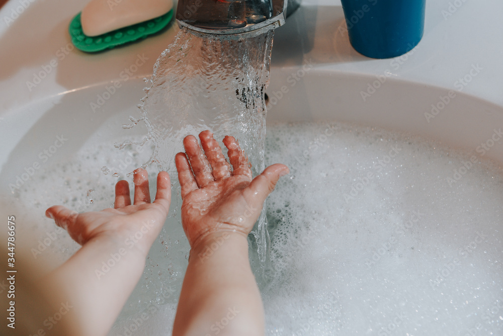 Fototapeta premium Cute little toddler girl washing her hands in a bathroom. Hygiene concept showing prevention of infection and viruses such as flu and covid-19