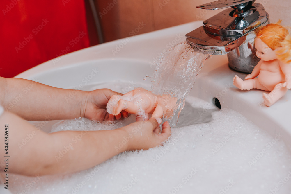 Fototapeta premium Cute little toddler girl washing her doll in a bathroom. Hygiene concept showing prevention of infection and viruses such as flu and covid-19