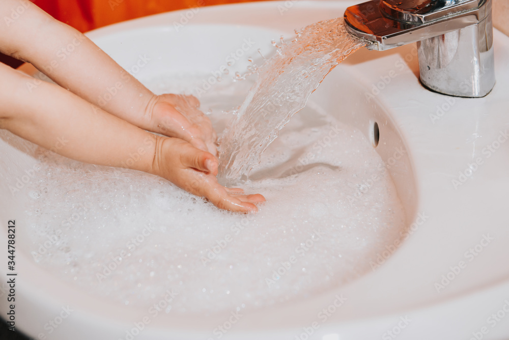 Fototapeta premium Cute little toddler girl washing her hands in a bathroom. Hygiene concept showing prevention of infection and viruses such as flu and covid-19