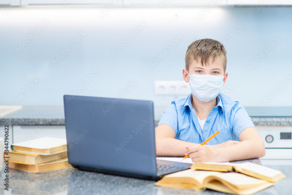 A boy with a face mask sitting on his laptop at home. The child is educated remotely during quarantine. Remote Learning During a Pandemic Concept A boy with a face mask sitting on his laptop at home. The child is educated remotely during quarantine. Remote Learning During a Pandemic Concept