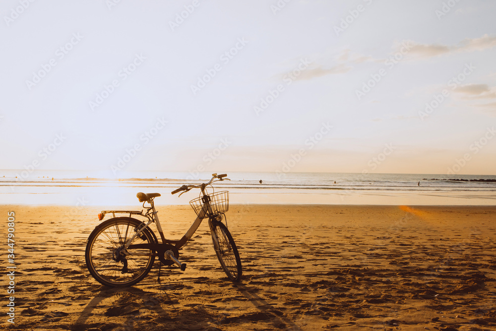 Fototapeta premium Bicycle on the ocean beach on sunset, warm orange colours