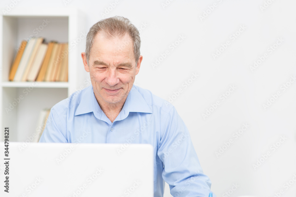 An elderly man works remotely behind a laptop at home. An elderly man works remotely behind a laptop at home.
