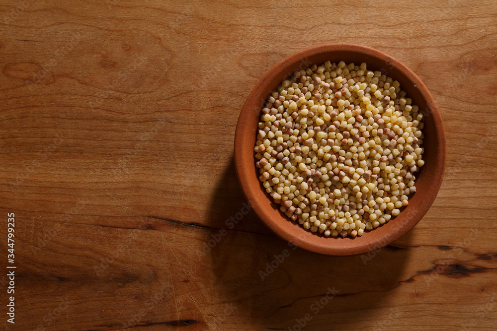 Fregola sarda dentro ciotola in ceramica, sopra tavolo di legno Fregola sarda dentro ciotola in ceramica, sopra tavolo di legno