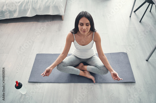 Pleased young female person sitting on yoga mat photo