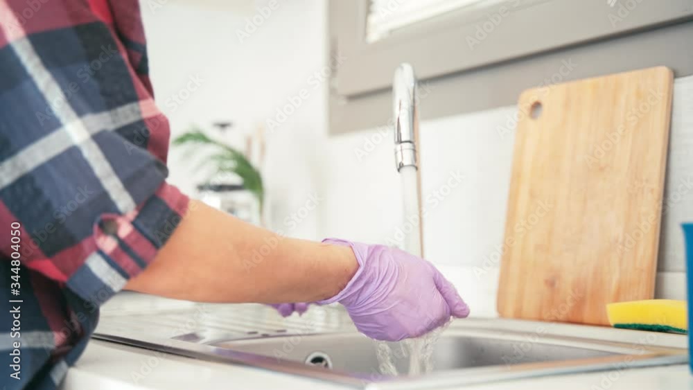 Close-up shot of woman's hands in protective latex gloves washing a rag in the sink in the kitchen. Close-up shot of woman's hands in protective latex gloves washing a rag in the sink in the kitchen.