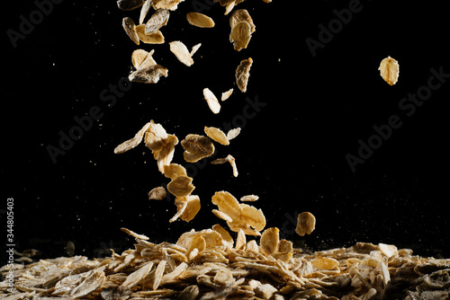 Whole oats being poured onto counter, oatmeal on a black background