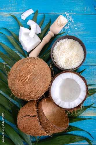 Whole coconut nut, shell, coconut flakes, green palm leaves on a blue wooden background. Top view, flat lay. Tropical theme.
