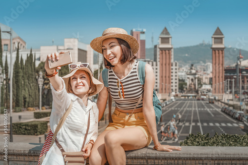 Two girl friends enjoy each others company on the streets of Barcelona and take a selfie photo on their smartphone