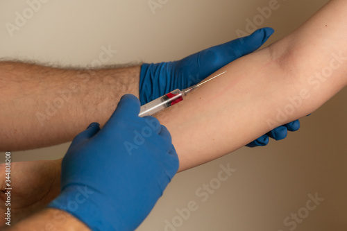 a doctor in disposable gloves takes blood from a patient’s vein for analysis