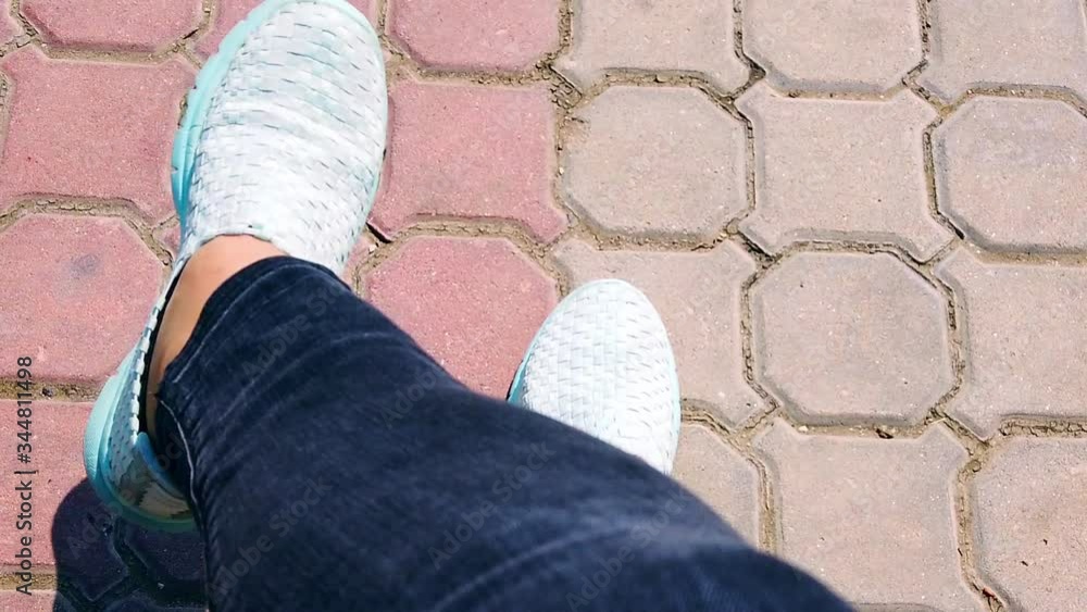 Female legs in black jeans on background of gray street pavers. woman moves her legs in blue speed shoes, sneakers. Close-up. Slow motion. Female legs in black jeans on background of gray street pavers. woman moves her legs in blue speed shoes, sneakers. Close-up. Slow motion.