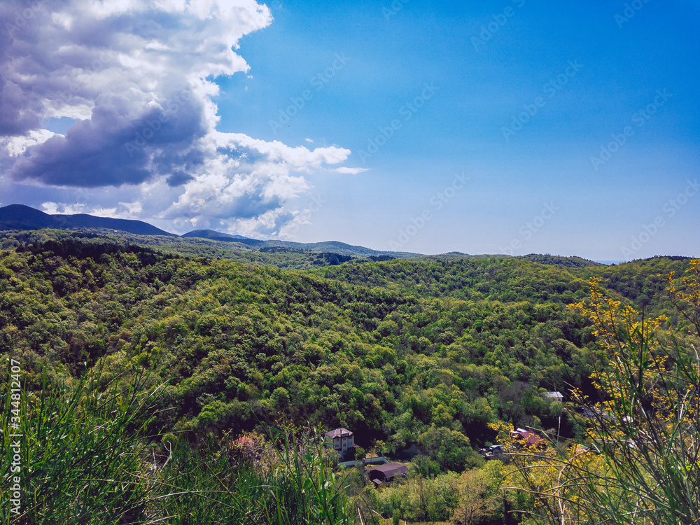Mountains covered with green vegetation on a sunny day against a blue cloudy sky.