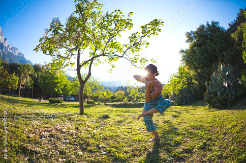 The girl practices yoga on the green grass on a background of green trees and mountains.