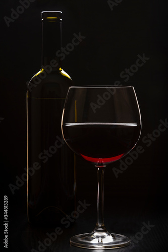 a glass and a bottle of wine standing on the table. vertical orientation on a dark background.