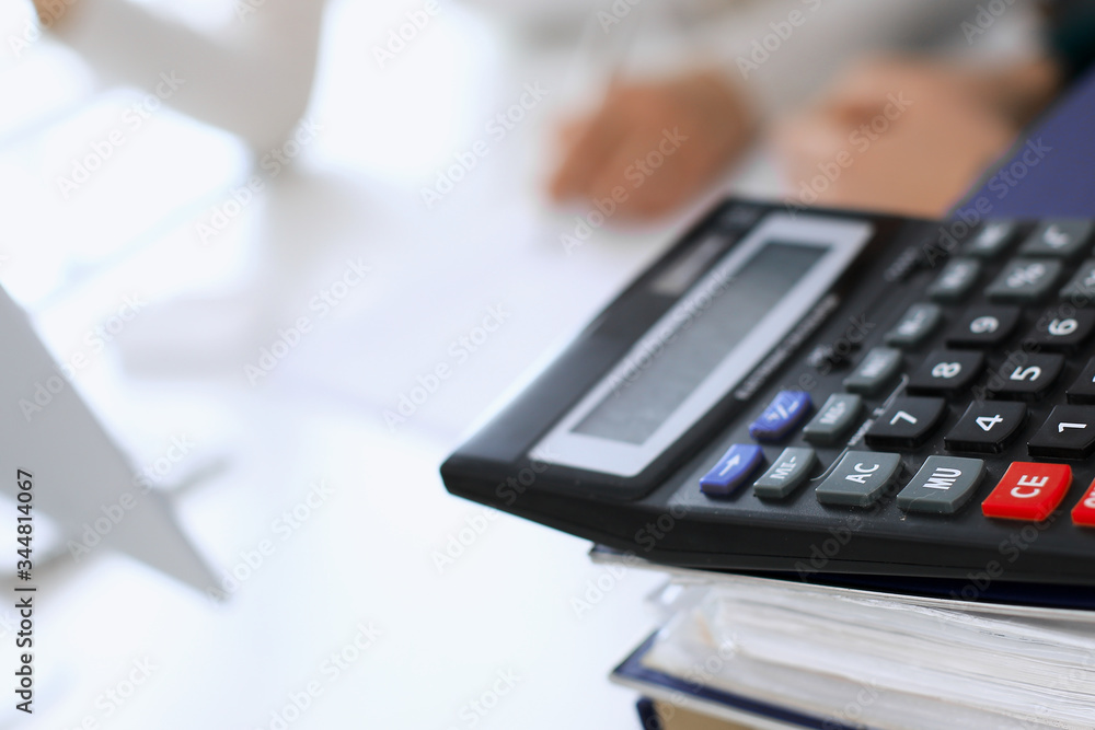 Calculator and binders with papers are waiting to be processed by business woman or bookkeeper working at the desk in office back in blur. Internal Tax and Audit concept Calculator and binders with papers are waiting to be processed by business woman or bookkeeper working at the desk in office back in blur. Internal Tax and Audit concept