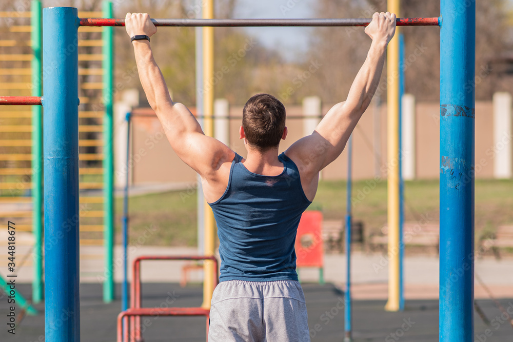 Fototapeta premium Young strong guy pulls himself up on the horizontal bar.