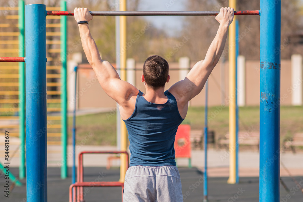 Young strong guy pulls himself up on the horizontal bar.