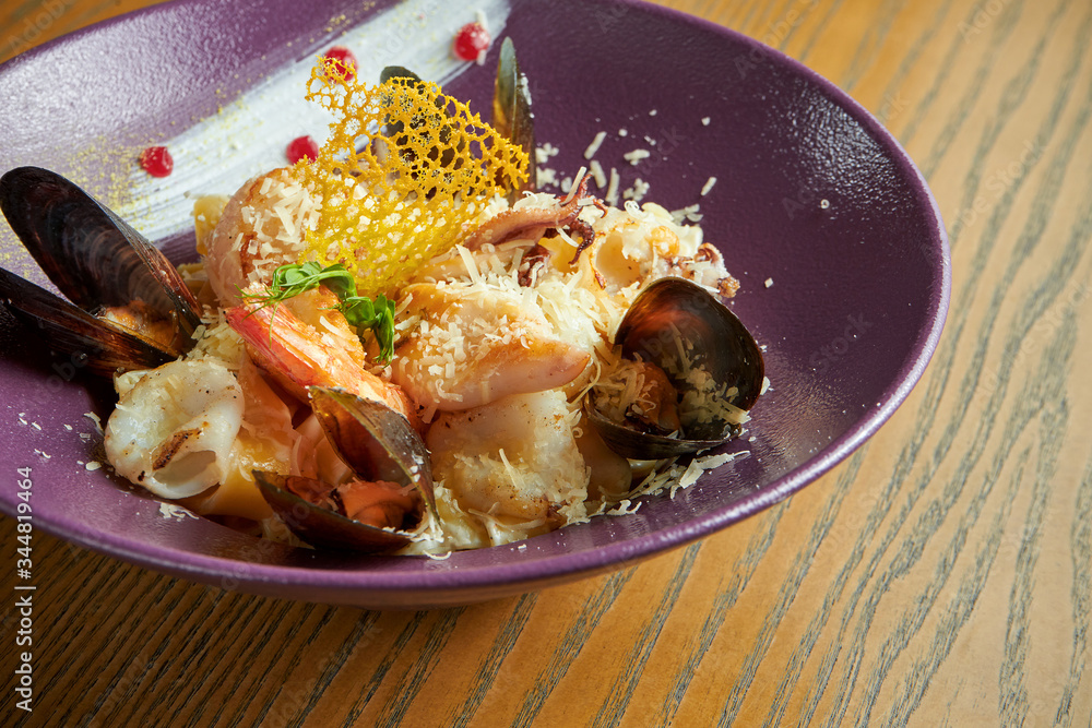 Homemade fettuccine pasta with seafood - squid, mussels and large shrimps in a purple bowl on a wooden background. Close up view Homemade fettuccine pasta with seafood - squid, mussels and large shrimps in a purple bowl on a wooden background. Close up view