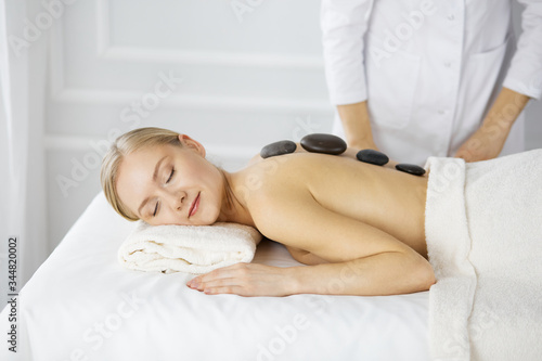 Beautiful caucasian woman enjoying warm stones procedure with closed eyes. Beauty and Spa salon concept